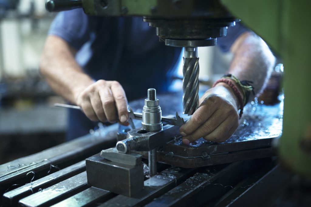 Trabalhador operando uma fresadora em oficina metalúrgica, ajustando peça com precisão